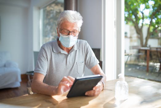Elderly man wearing face mask using tablet at home, reflecting on technology and health precautions.